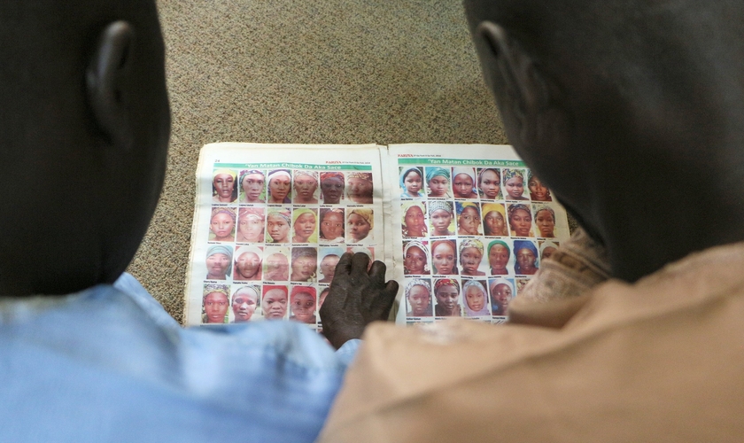 Dois pais de meninas Chibok olham retratos de algumas das meninas sequestradas por Boko Haram em 2014. (Foto: Reprodução / Portas Abertas UK)