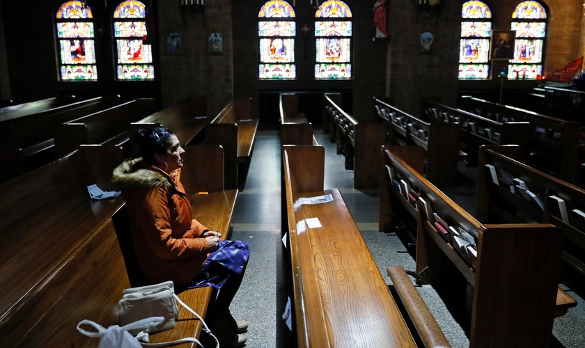 Mulher sentada no banco de uma Igreja Católica vazia em Des Moines, em Iowa, nos EUA. (Foto: Charlie Neibergall/Associated Press)