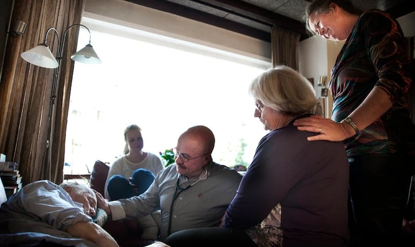 A família e o médico Sjef Boesten (com estetoscópio) se reúnem enquanto a vida de Siep Pietersma se esvai (Foto: Mona van den Berg)