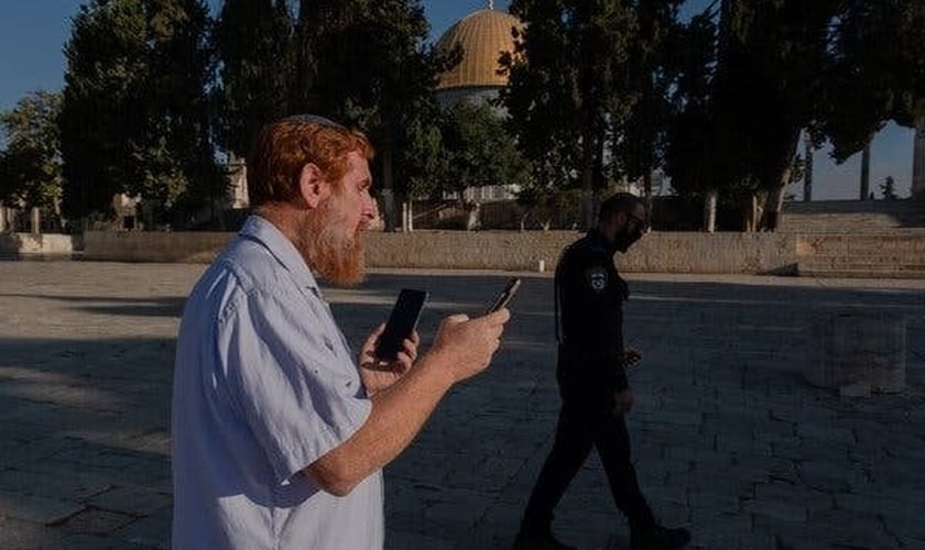 O rabino Yehudah Glick orando no Monte do Templo, em agosto de 2021, enquanto um policial patrulhava nas proximidades. (Foto: Amit Elkayam/The New York Times).