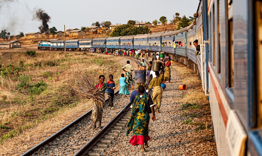 Multidões caminham ao lado de um trem estacionado na Zâmbia. (Foto: Katsuma Tanaka/Unsplash)