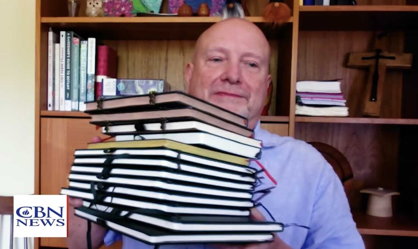 Don Ashley mostra os cadernos preenchidos à mão durante seu projeto de copiar todo o Novo Testamento. (Foto: CBN News)