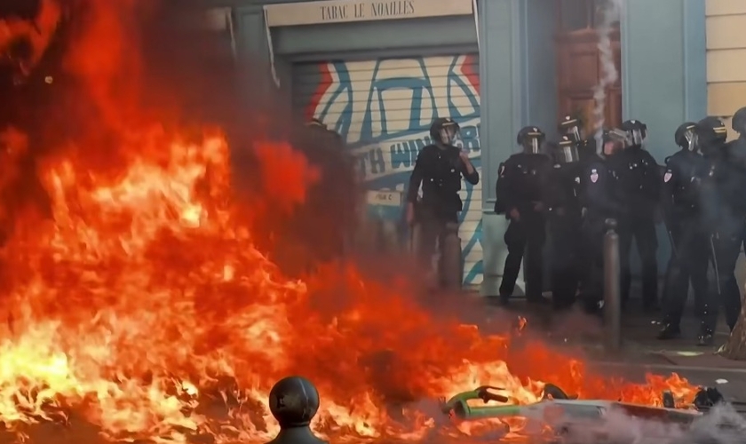 Incêndio durante protestos violentos na França, diante de policiais mobilizados para conter os distúrbios. (Captura de tela/CBS Pittsburgh)