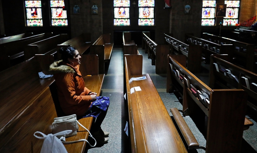Mulher sentada no banco de uma Igreja Católica vazia em Des Moines, em Iowa, nos EUA. (Foto: Charlie Neibergall/Associated Press)