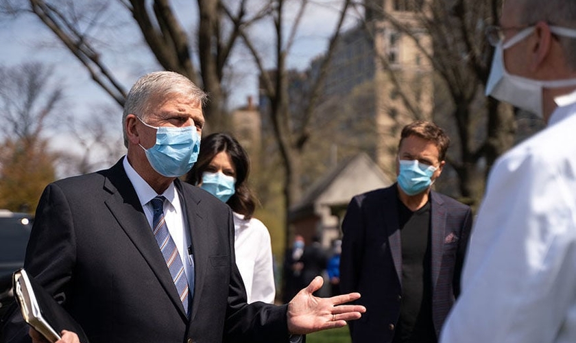 Usando máscaras, Pastor Franklin Graham (esquerda) é acompanhado do cantor Michael W. Smith (ao fundo) durante visita ao hospital de campanha montado pela Samaritan's Purse, organização missionária comandada pelo evangelista. (Foto: Samaritan's Purse)