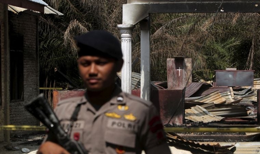 Policial segura rifle enquanto fica de guarda em frente a uma igreja queimada em Suka Makmur Village, em Aceh, Indonésia