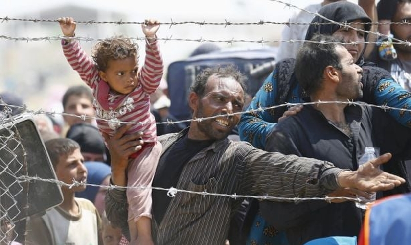 Refugiado sírio segura sua filha, enquanto tenta cruzar a fronteira da Turquia (Foto: Reuters)