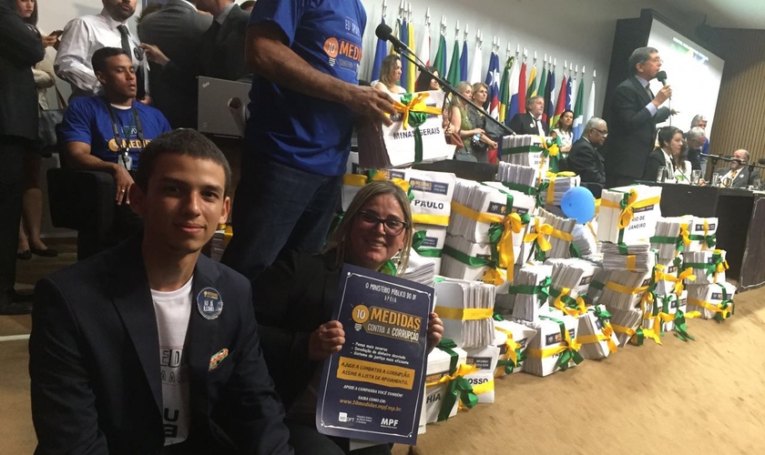 Marisa Lobo expõe logo das 10 Medidas Contra a Corrupção, enquanto o pastor Armando Bispo, da IBC Fortaleza, fala aos presentes no ato da entrega simbólica das assinaturas.