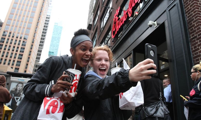 A jovem Jaimie Cranford (à direita) tira uma selfie com Mariah Reives (esquerda), exibindo sorrisos e seus lanches da rede lanchonetes fundadas por cristãos. (Foto: Tina Fineberg / AP Photo)