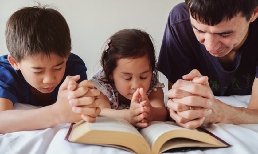 Pai lê a Bíblia com filhos. (Foto: Getty)