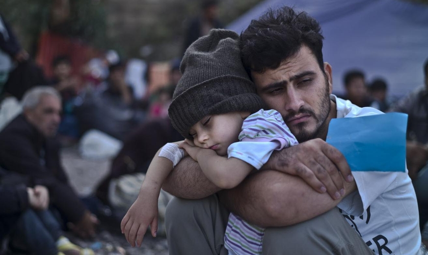 Refugiado sírio segura o filho nos braços em campo, na Turquia. (Foto: AP/Lefteris Pitarakis)