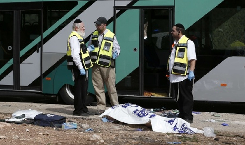 Forças de segurança israelenses conversam ao lado de corpo após ataque a tiros contra um ônibus próximo ao bairro palestino de Jabal Mukaber, em Jerusalém Oriental. (Foto: Thomas Coex/AFP)