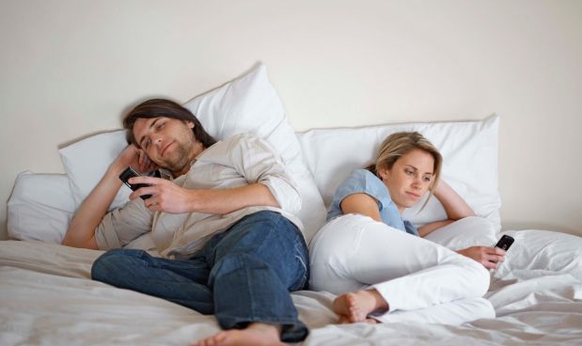 Casal usando celulares na cama. (Foto: Getty)