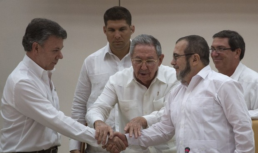 Presidente da Colômbia Juan Manuel Santos e o líder das FARC Timoleón Jiménez cumprem ato simbólico para acordo de paz, na frente do presidente cubano Raúl Castro (Foto: AP Photo / Desmond Boylan)