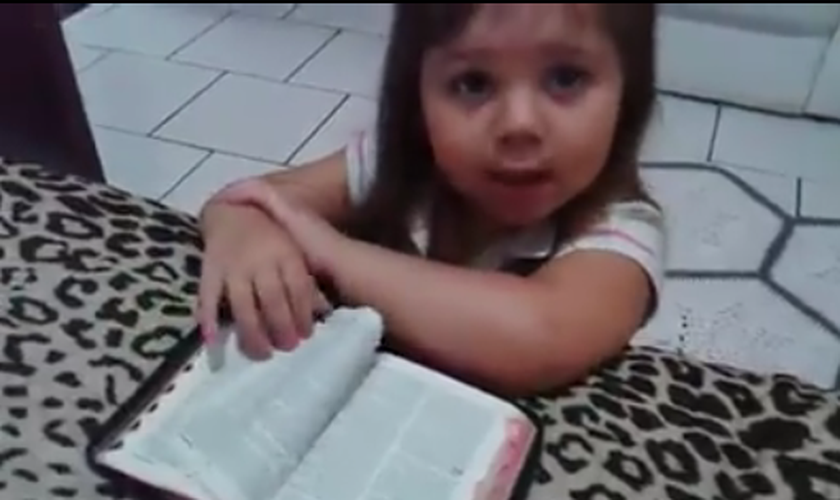 Ajoelhada em frente a uma cama, com os braços apoiados sobre uma Bíblia, a menina inicia suas preces. (Foto: Reprodução)