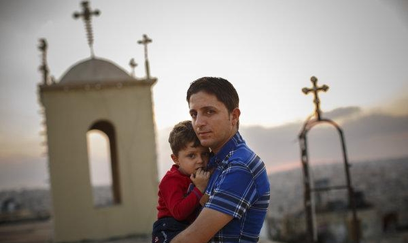 Homem cristão segurando seu filho, enquanto muitos de seus vizinhos fugiram da violência no Iraque. (Foto: Warrick Page/New York Times)