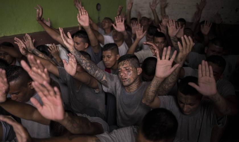 Antigos membros de gangues, presos na cadeia de Gotera, levantam as mãos durante o culto. (Foto: Victor Peña/El Faro)
