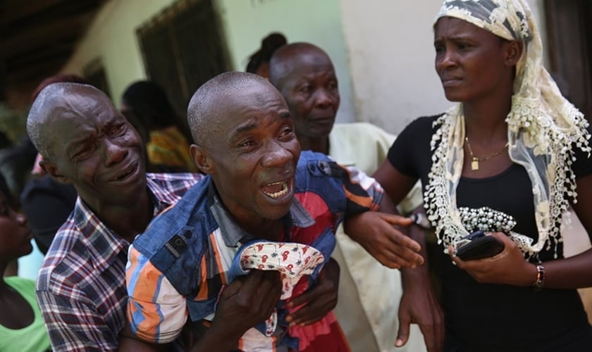 Liberiano chora enquanto o corpo de sua esposa Ã© levado por uma equipe mÃ©dica na Ãfrica. (Foto: John Moore/Getty Images)