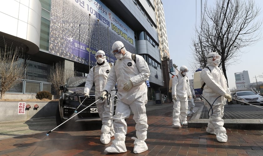 Trabalhadores com equipamento protetor usam desinfetante em spray contra o novo coronavírus em frente à igreja em Daegu, na Coreia do Sul, nesta quinta-feira (20). (Foto: Kim Jun-beom/Yonhap via AP)