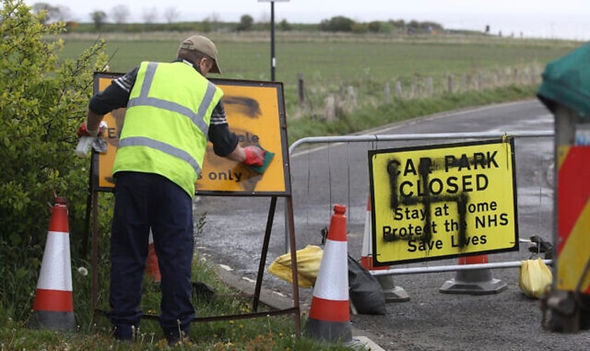 Trabalhador remove suástica pintada em uma placa na entrada de uma estrada fechada e parque de estacionamento perto do farol de Whitley Bay, em Northumberland, Inglaterra, quinta-feira, 30 de abril de 2020. (Foto: Owen Humphreys / AP)