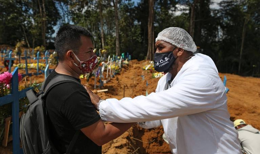O pastor Izaías Nascimento conforta um jovem durante o funeral de seu pai. (Foto: Michael Dantas/AFP)
