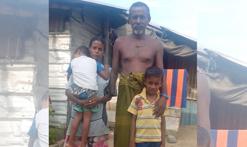 Khanjana ao lado da esposa e dois filhos, em frente à cabana da família. (Foto: Gospel For Asia)