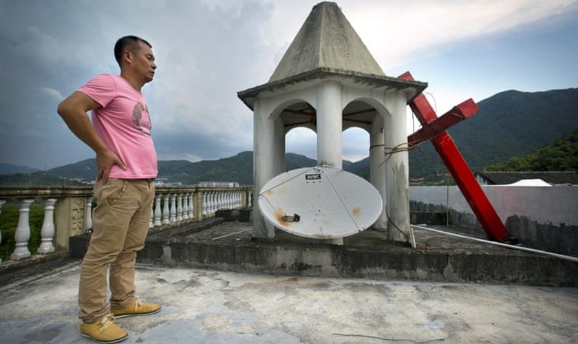 Líder de igreja permanece em pé no teto do templo, após o local ter sua cruz removida, na província de Zhejiang. (Foto:  Mark Schiefelbein/AP)