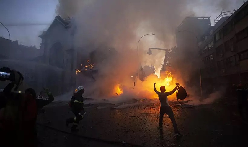 Homem comemora em frente a igreja destruída em Santiago. (Foto: Claudio Reyes / AFP)