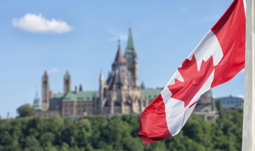 Bandeira canadense, com o parlamento ao fundo. (Foto: Reprodução / Shutterstock)