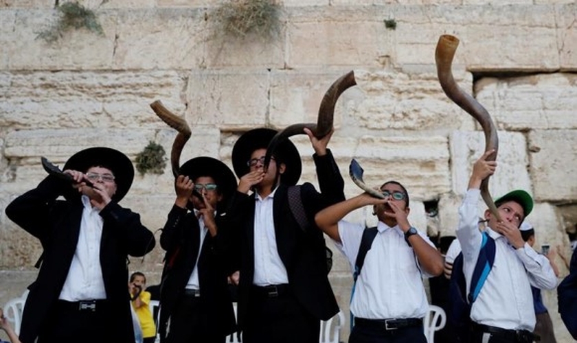 Judeus ultraortodoxos tocam o shofar enquanto os fiéis oram no Muro das Lamentações. (Foto: Reprodução / El País)