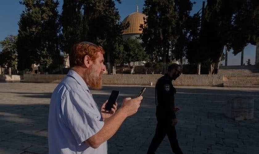 O rabino Yehudah Glick orando no Monte do Templo, em agosto de 2021, enquanto um policial patrulhava nas proximidades. (Foto: Amit Elkayam/The New York Times).