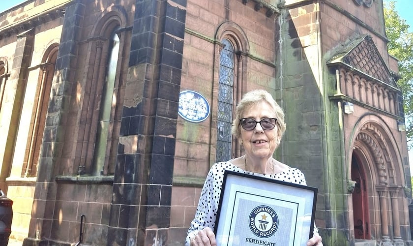 Pam Knowles em frente à igreja segura sua placa do Guinness Book. (Foto: Facebook/St. Anne’s, Aigburth)