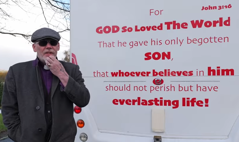 Pastor Mick Fleming ao lado de sua van, que traz o versículo bíblico João 3:16. (Captura de tela/YouTube/Church on the Street Ministries)