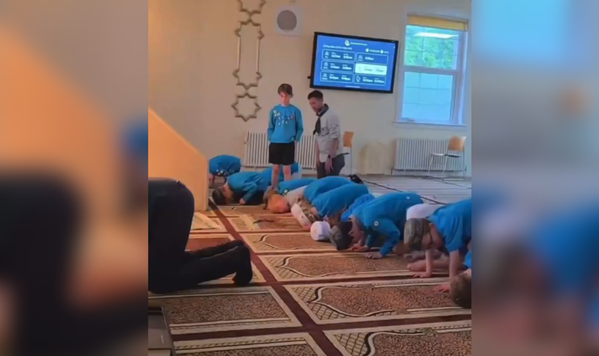 Jovem permanece em pé enquanto os demais participantes se ajoelham durante oração islâmica em mesquita. (Captura de tela/X/@megbasham)