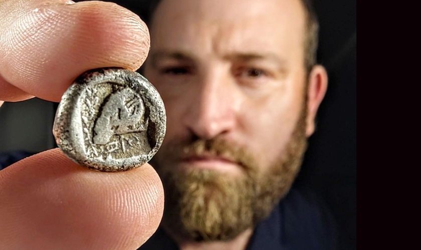 Yanniv David Levy, especialista em moedas da Autoridade de Antiguidades de Israel, segura a rara moeda de cerca de 2.500 anos. (Foto: Shai Halevi/Autoridade de Antiguidades de Israel)