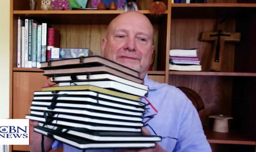 Don Ashley mostra os cadernos preenchidos à mão durante seu projeto de copiar todo o Novo Testamento. (Foto: CBN News)