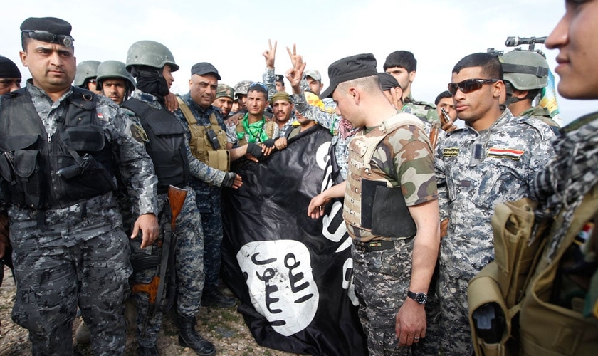 Homens da polícia iraquiana e combatentes xiitas seguram uma bandeira Estado Islâmico.