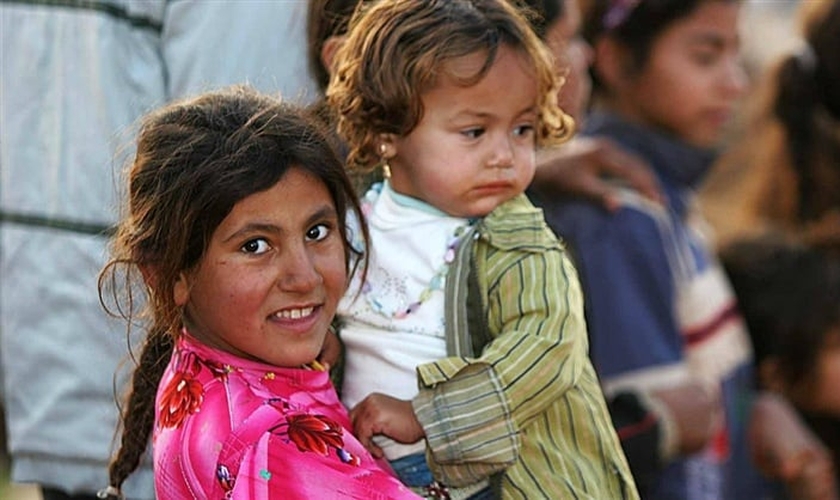Garota síria segura bebê no colo, em campo de refugiados.